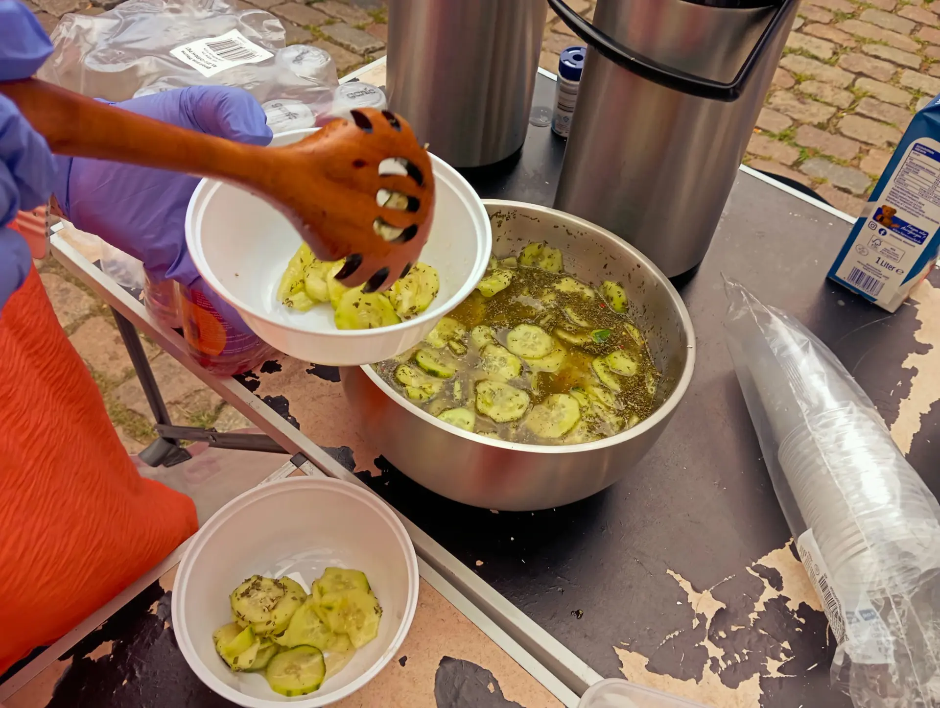 Helferin füllt Gurkensalat in Schalen ab